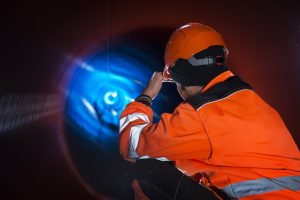 Pipeline construction worker in reflective protective uniform inspecting pipe tube for natural gas distribution.